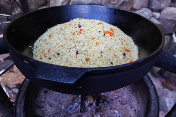 Rice pilaf in a large cast-iron cauldron on fire