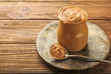 Jar with tasty peanut butter on wooden table