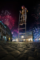 Night street circus performance whit clown balanced in ladder. Festival city background. fireworks...
