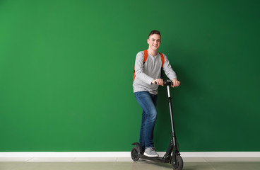 Teenage boy with kick scooter near color wall