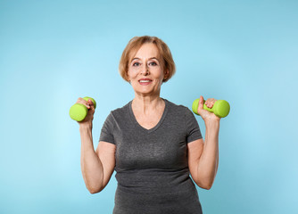 Beautiful mature woman with dumbbells on color background