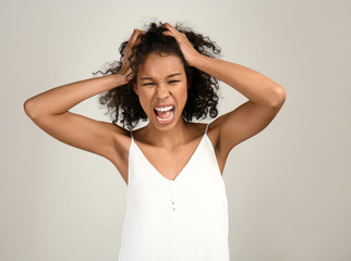 Fototapeta premium Frustrated young woman with curly hair screaming and grabbing head, expressing stress, anger, and emotional distress