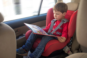 Toddler boy reading book in child car seat