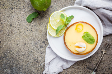 Key lime tarts with fresh lime and mint leaves, top view