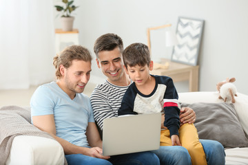 Happy gay couple and adopted child with laptop at home