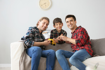 Happy gay couple playing with adopted child at home