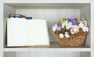 Artificial rose flower in basket on the bookshelf in library against blur of open hardcover book.