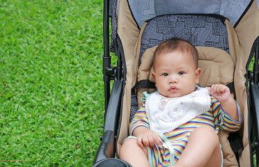 Fototapeta na wymiar Close-up little Asian baby boy sitting in the stroller at the green garden. 