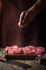 Man cooking meat steaks on kitchen. Chef salt and pepper meat on wooden background