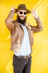 Portrait of a stylish bearded man dressed in jacket and hat on the bright yellow background outdoors