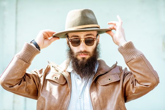 Portrait of a stylish bearded man wearing hat on the light turquoise background outdoors