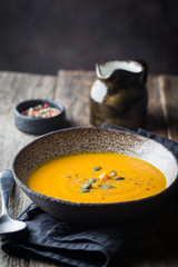 Vegetarian autumn pumpkin cream soup with seeds on wooden background