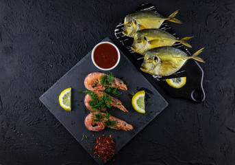Boiled shrimps and smoked fish with lemons, greens and sauce on a wooden background. Top view