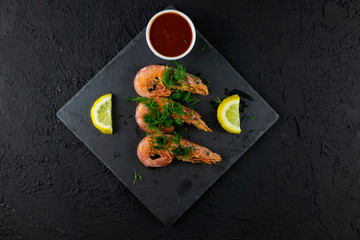 Boiled shrimps with lemons, greens and sauce on a wooden background. Top view
