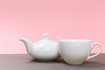 vintage white porcelain teapot and cup on a gray board and pink background