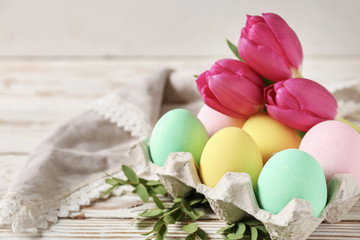 Package with beautiful Easter eggs and flowers on white wooden table