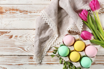 Package with beautiful Easter eggs and flowers on white wooden table