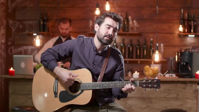 Young man performs a song on an acoustic guitar. Man plays a guitar in front of a bar counter. Singing a song in a small restaurant.