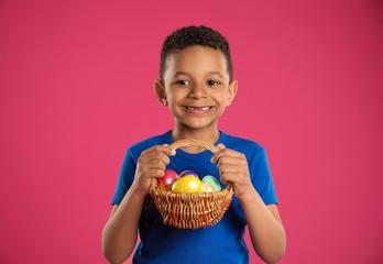 Little African-American boy with basket of Easter eggs on color background