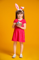 Little girl with Easter eggs and bunny ears on color background