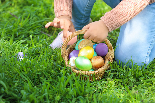 Little girl gathering Easter eggs in park, closeup
