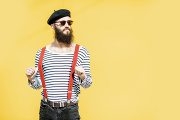 Portrait of a stylish bearded man dressed in striped shirt, suspenders and hat on the yellow...