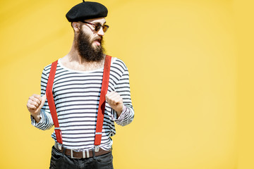 Portrait of a stylish bearded man dressed in striped shirt, suspenders and hat on the yellow...