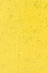 Blurred abstract background. The texture of a painted concrete rough surface with cracks and irregularities bright yellow. Cropped shot, vertical, place for text, nobody. Design concept.