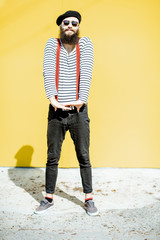 Full body portrait of a stylish bearded man dressed in striped shirt, suspenders and hat on the...