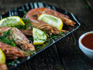 Boiled shrimps with lemons, greens and sauce on a wooden background. Side view