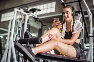 Fototapeta na wymiar Young attractive woman listening to music by earphones connect to smart phone or cellphone. Relaxation after hard workout in gym 