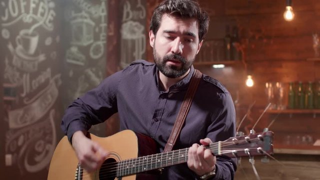 Man plays a rythm on an acoustic guitar at a solo concert. Young man performing a composition on an acoustic musical instrument.