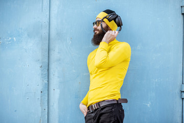 Portrait of a stylish bearded man in yellow clothes enjoying music with headphones on the blue background
