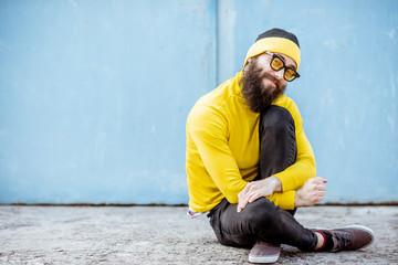 Portrait of a stylish man in yellow sweater sitting on the blue wall background outdoors