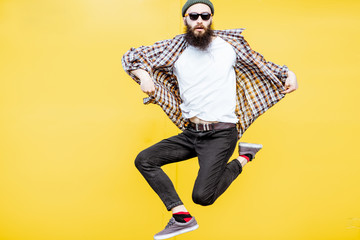 Portrait of a cool stylish man in checkered shirt jumping on the bright yellow background