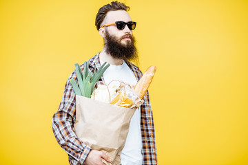 Portrait of a bearded man standing with shopping paper bag full of food on the bright yellow background