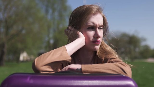Sad traveler missed her flight and bus - Sitting on her luggage suitcase and crying - Emotions of a white caucasian female woman with light long hair wearng bra and beige jacket