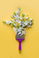 Creative concept white blooming fruit tree as paint seasons by paintbrush on yellow. View from above.