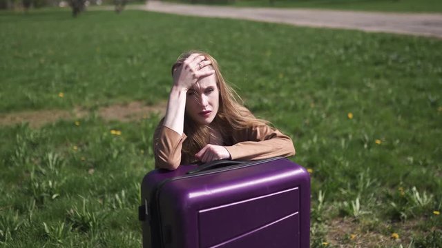 Sad traveler missed her flight and bus - Sitting on her luggage suitcase and crying - Emotions of a white caucasian female woman with light long hair wearng bra and beige jacket