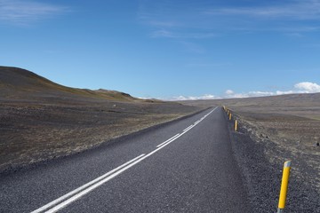 Endless straight asphalt road in barren wide landscape with yellow roadside markers into nowhere, Iceland