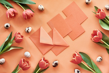 Fototapeta na wymiar Easter flat lay on orange paper with tulips, quail eggs, greeting cards and envelopes