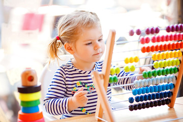 Adorable cute beautiful little toddler girl playing with educational wooden rainbow toy pyramid and counter abacus. Healthy happy baby learning to count and colors, indoors on sunny day. - obrazy, fototapety, plakaty