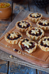 Mini Tartlets with dried fruits and nuts. Shortbread cookies with fruits stuffing on wooden background. Small sweet pie. Copy Space.