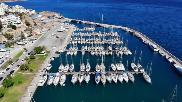 Aerial shot of yachts in marina, many vessels moored at shelter at Agios Nikolaos city, North-East Crete island shore. Camera fly back and up, reveal wider view of small vessels port