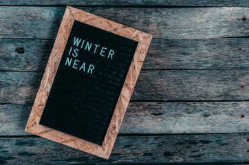 Letter board with white lettering winter is coming on old wooden background.