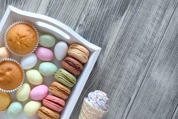 Easter flat lay with macarons, muffins and marzipan eggs jn a decorative tray on grey wood