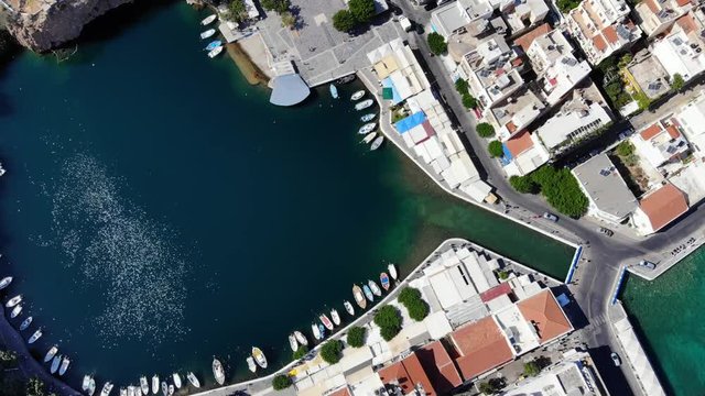 Voulismeni lake and channel to sea, buildings on shores, top-down aerial view of famous Cretan landmark at Agios Nikolaos city. Small boats moored at banks, shimmering water of circular shaped lagoon