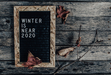 Letter board with white lettering winter is coming on old wooden background. Branch and fallen...