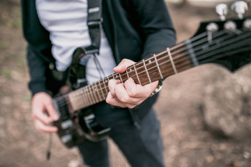 Fototapeta na wymiar A man plays power chords on a black electric guitar outdoors - hard rock music