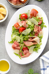 Salad with jamon (parma, ham, serrano, prosciutto), parmesan cheese, lettuce, cherry tomatoes on a plate. Delicious lunch, healthy food, Italian (spanish) cuisine